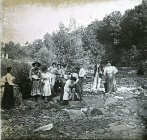 Retrat de grup de cos sencer de diversos membres de la família Bassols, vora un riu. Al centre, assegut, en segon terme, l'advocat Joan Bassols, i, a la dreta, amb barret, la seva filla Mercè Bassols.